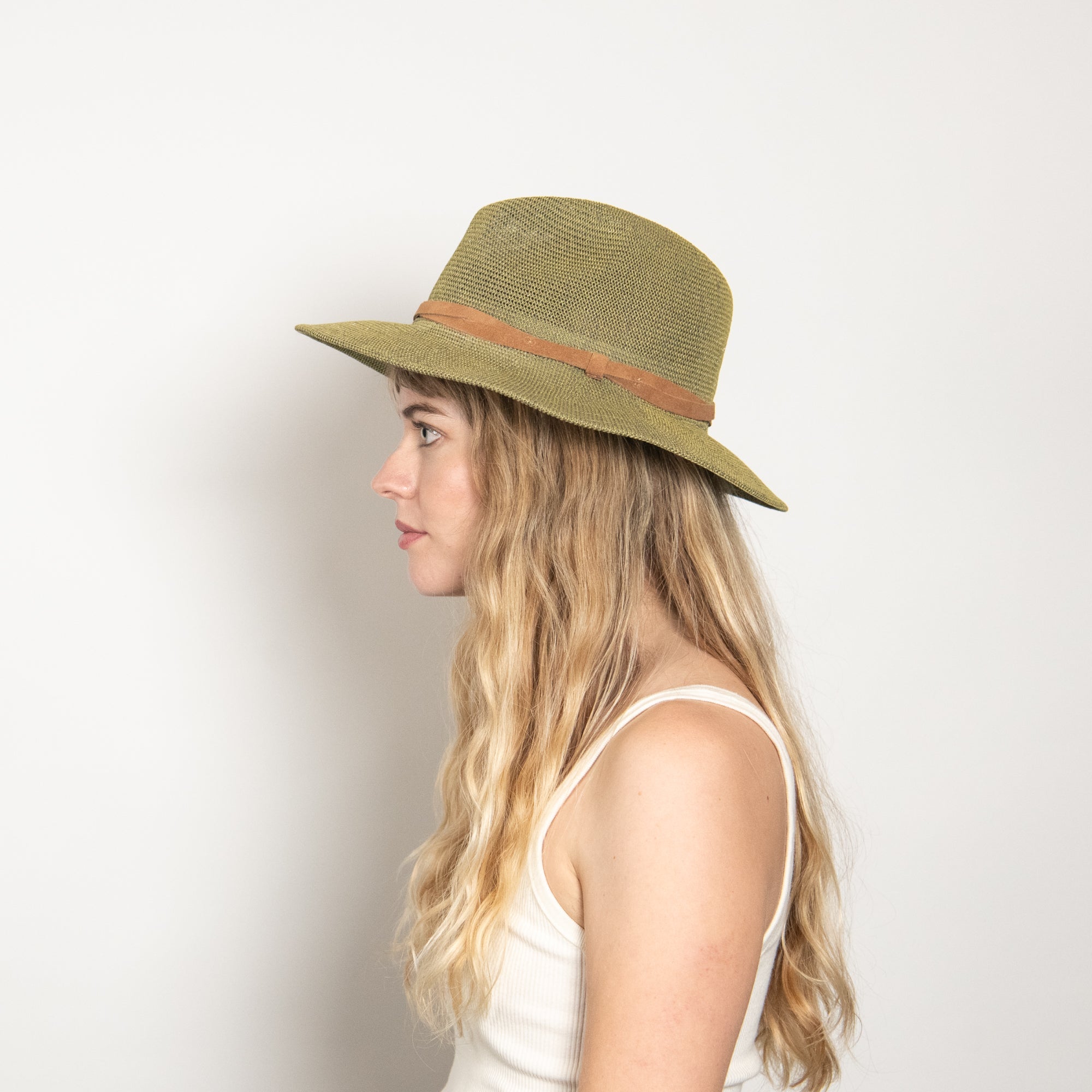 Woman wearing a green straw hat with a brown band on a light background