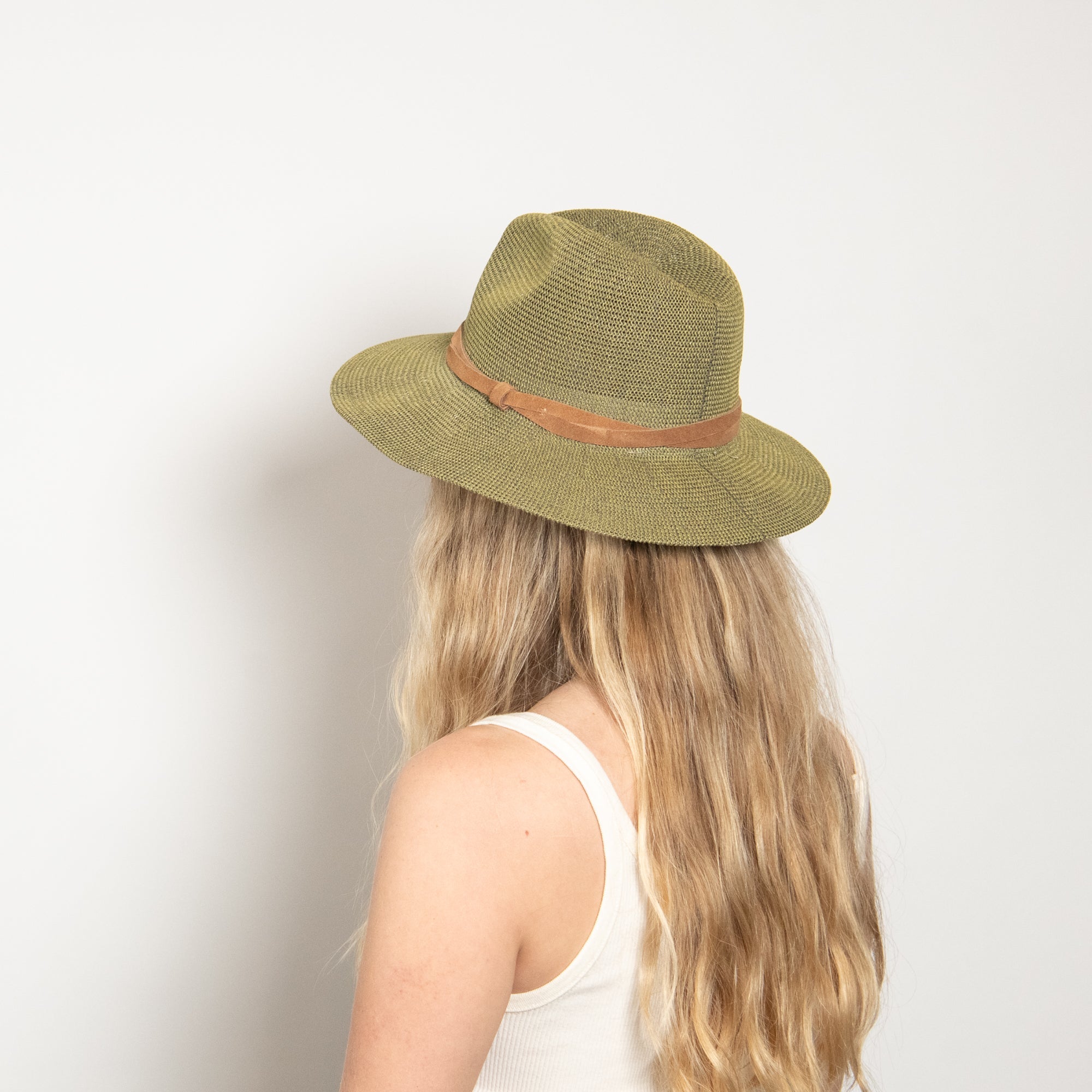 Person wearing a green straw hat with a brown band on a plain background