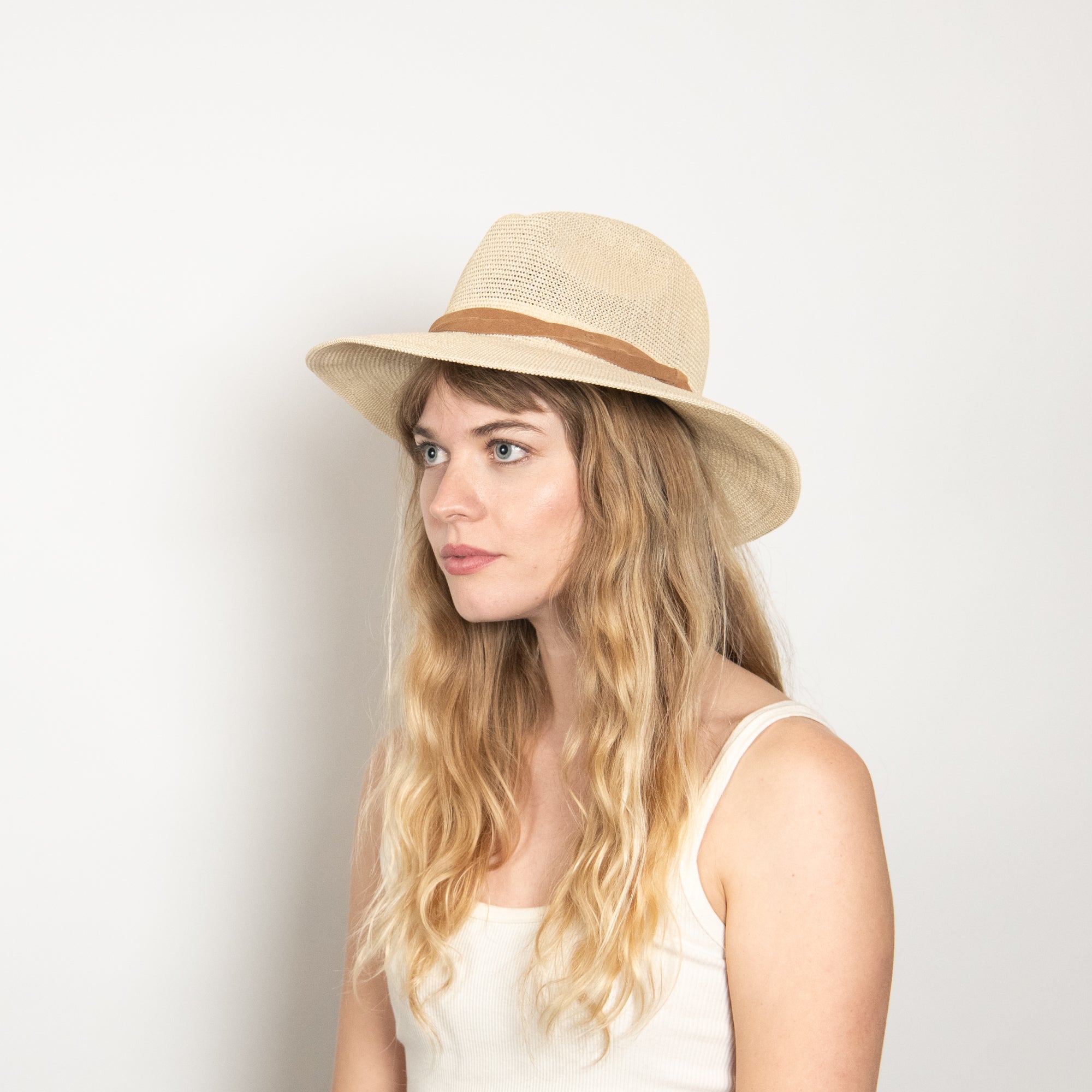 Woman wearing a beige straw hat with a brown band on a light background