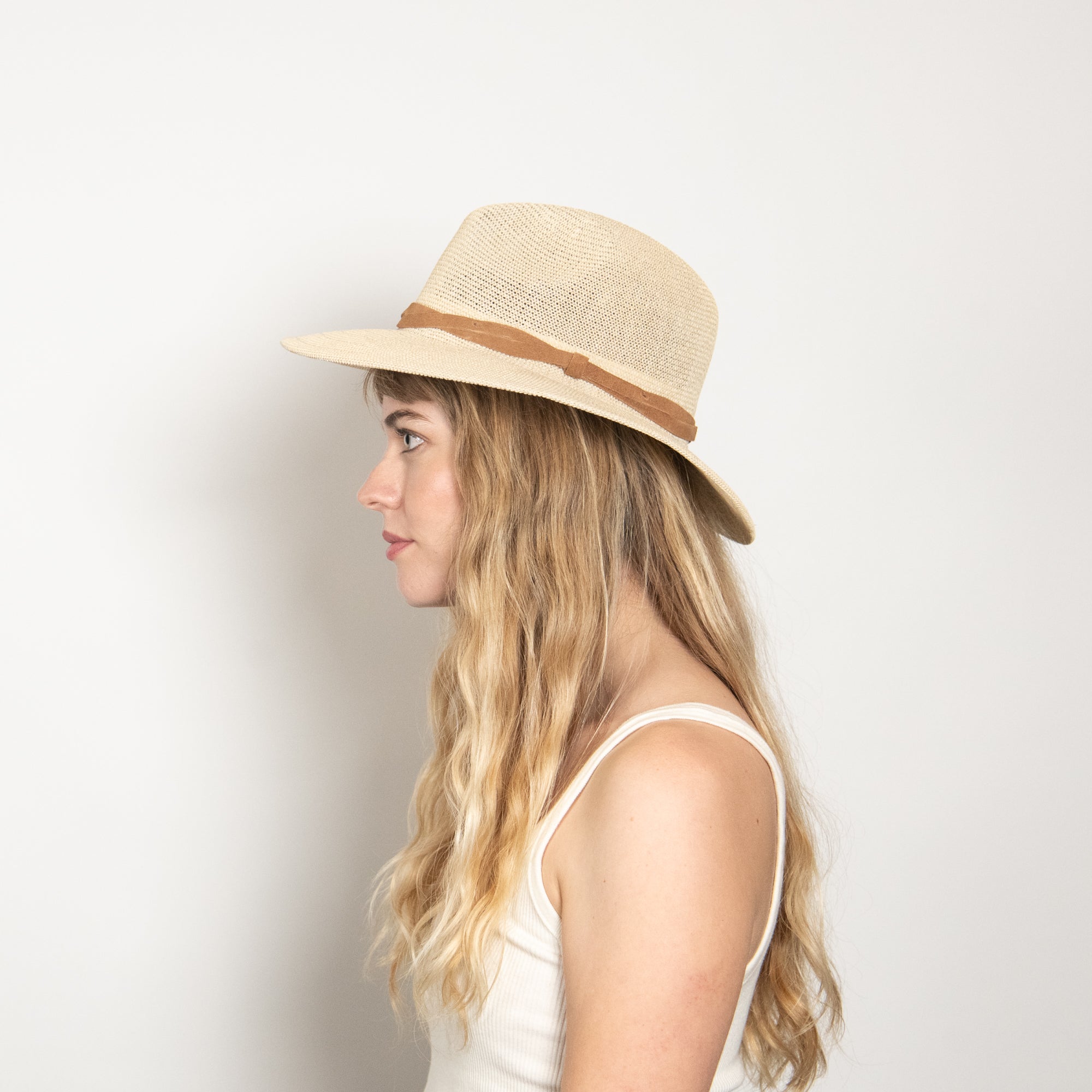 Woman wearing a straw hat with a brown band on a plain background