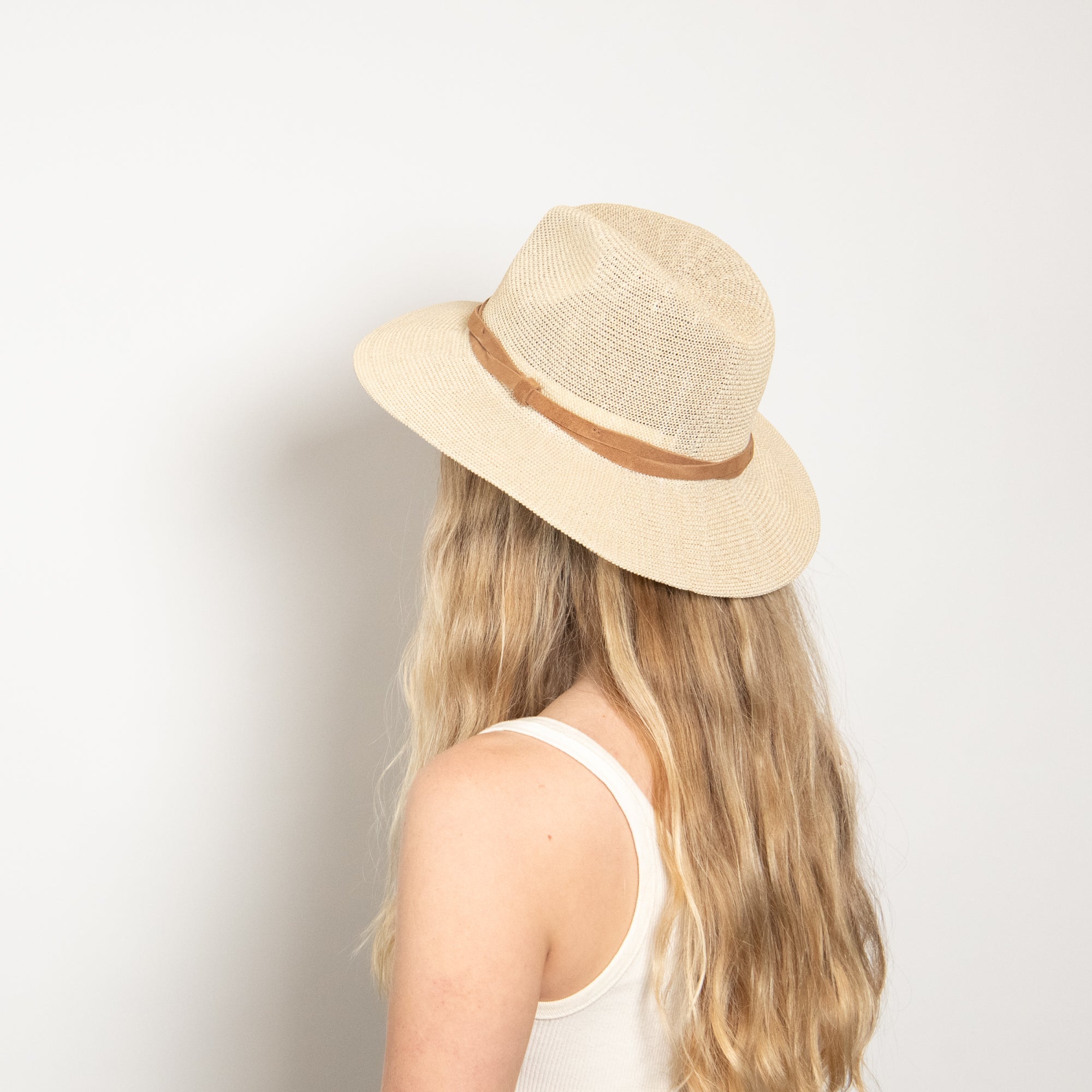 Person wearing a beige straw hat with a brown band on a light background