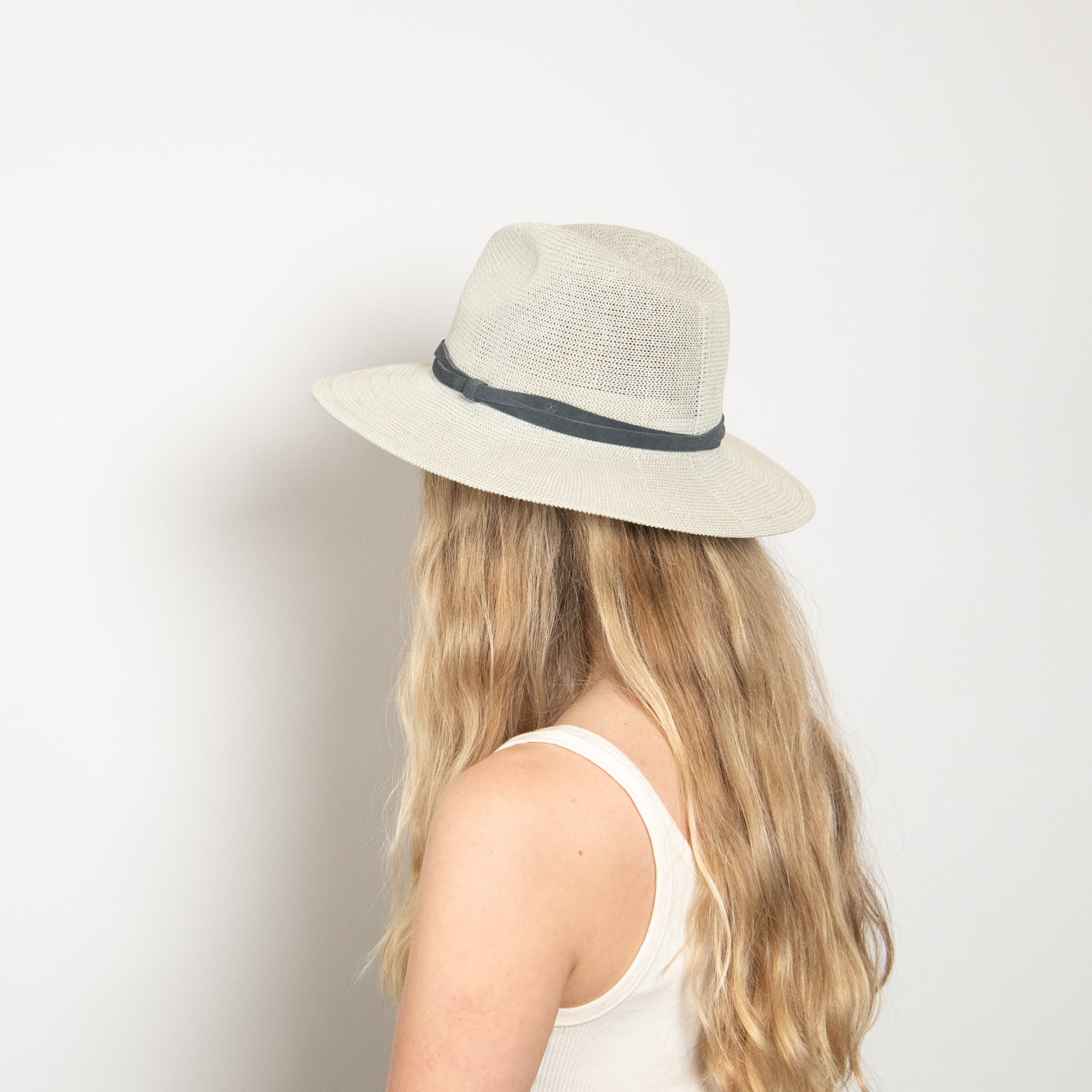 Person wearing a beige hat with a dark band on a plain background