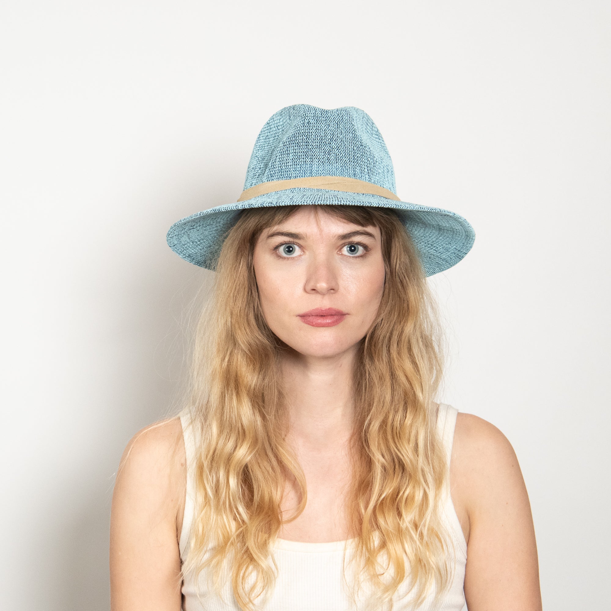 Woman wearing a light blue straw hat against a plain background