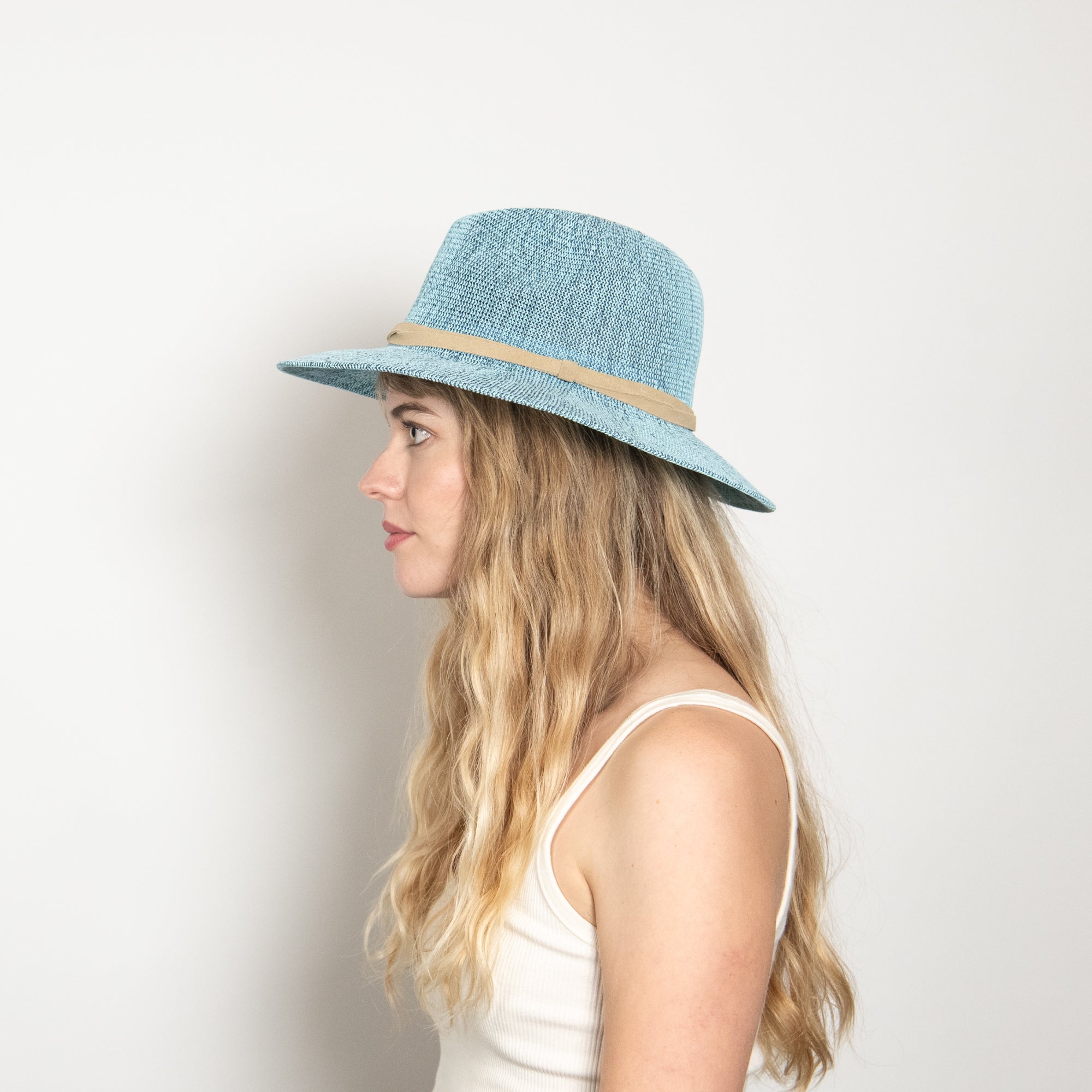 Woman wearing a light blue straw hat with a beige band on a white background