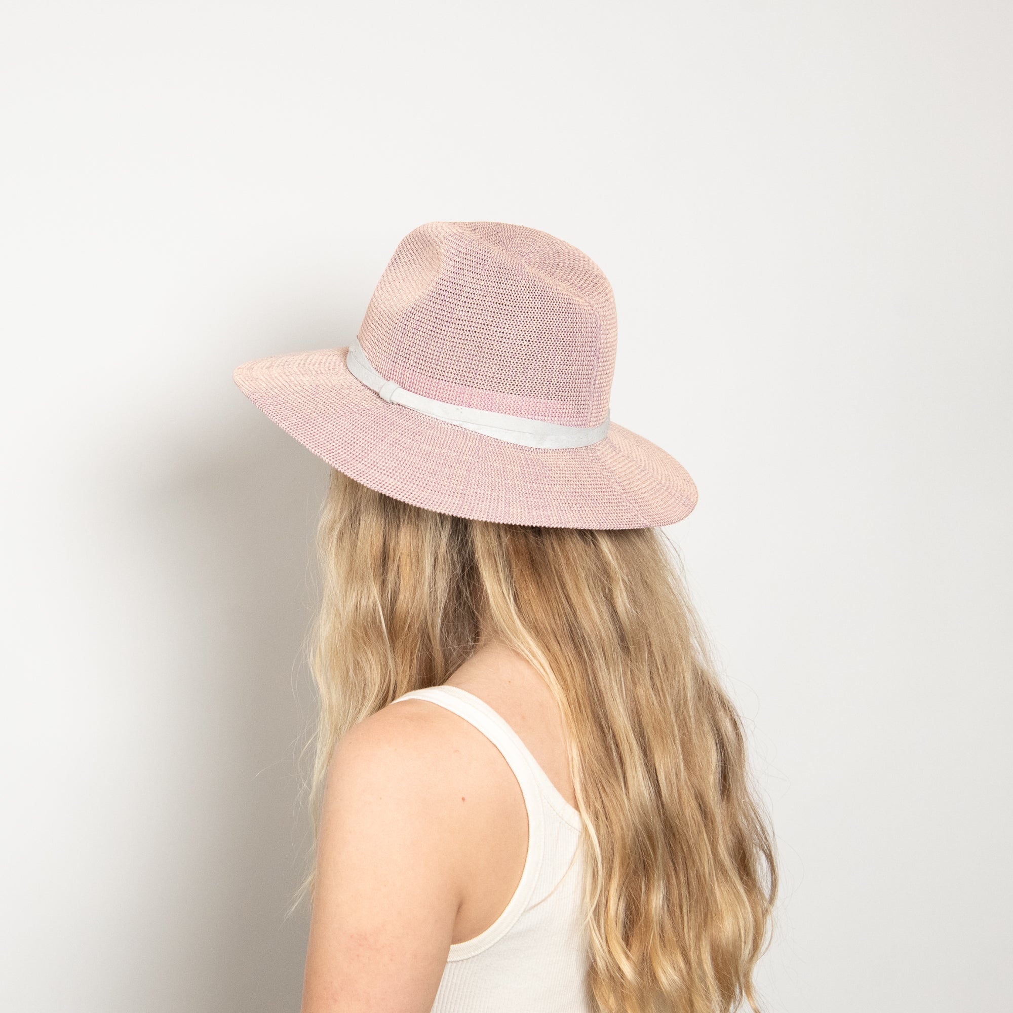 Person wearing a pink straw hat with a white band on a plain background