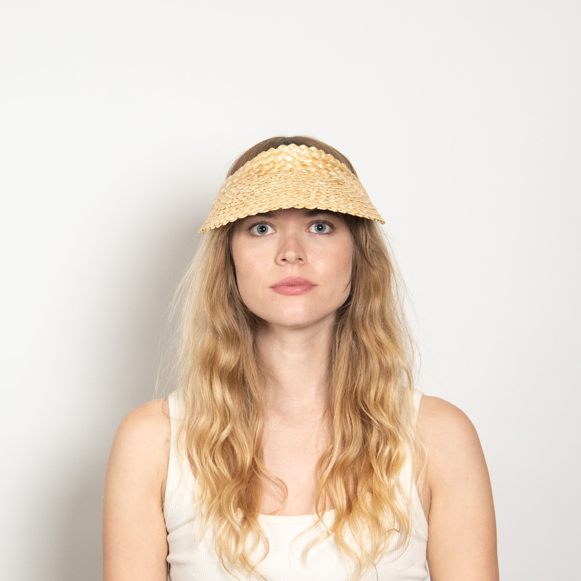 Woman wearing a straw visor against a plain background