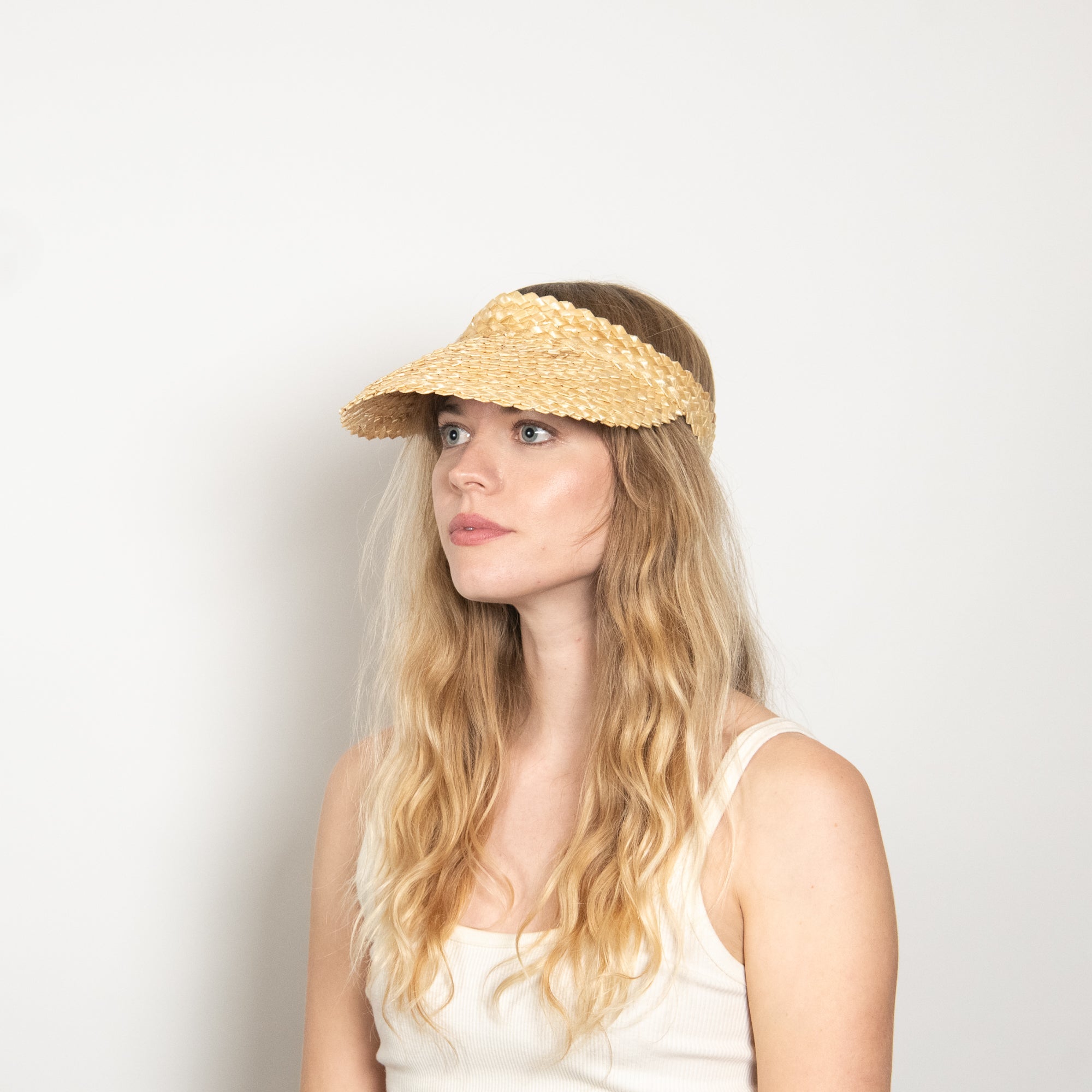 Woman wearing a straw visor against a plain background