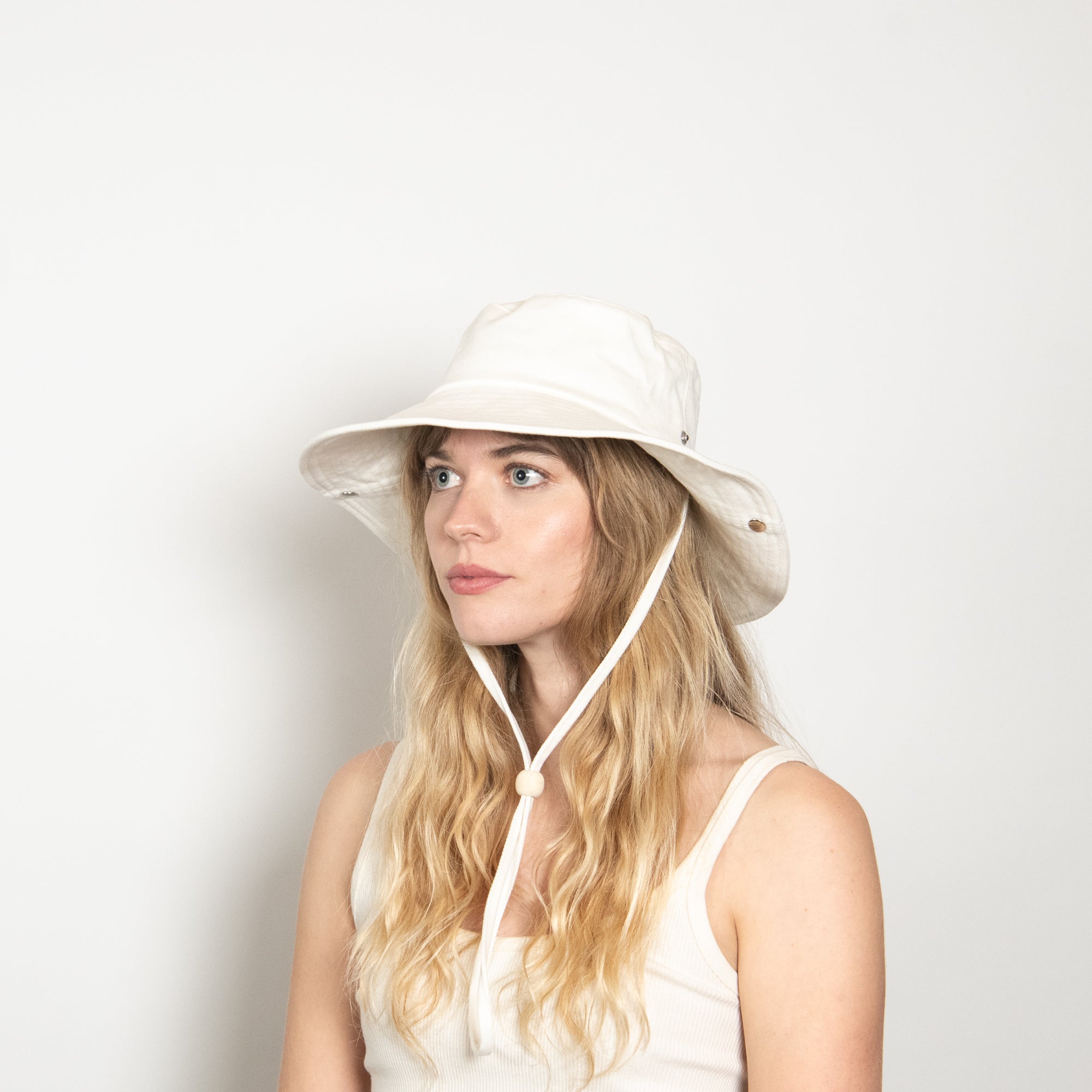 Woman wearing a white sun hat with a neck flap on a light gray background