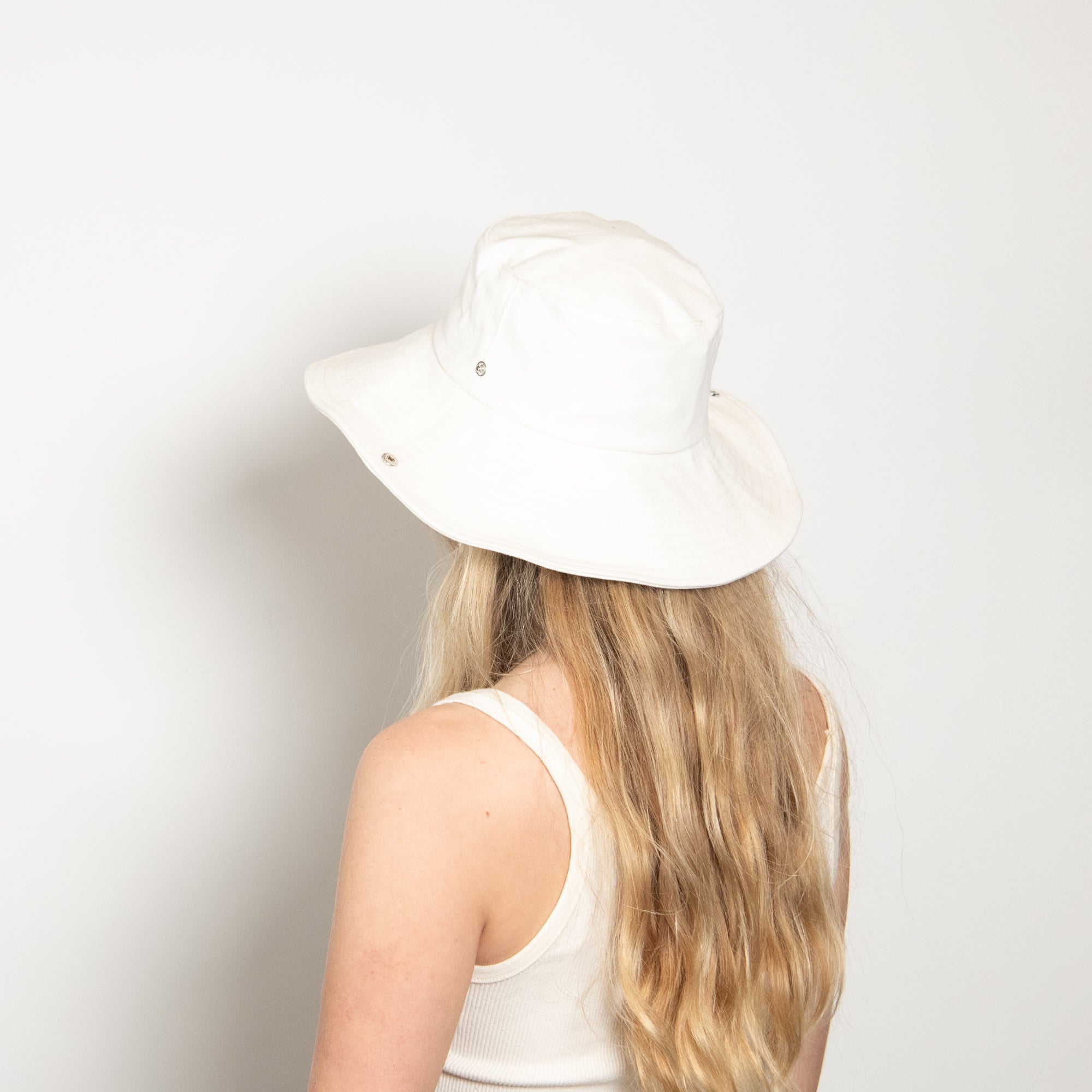 Person wearing a white bucket hat against a plain background
