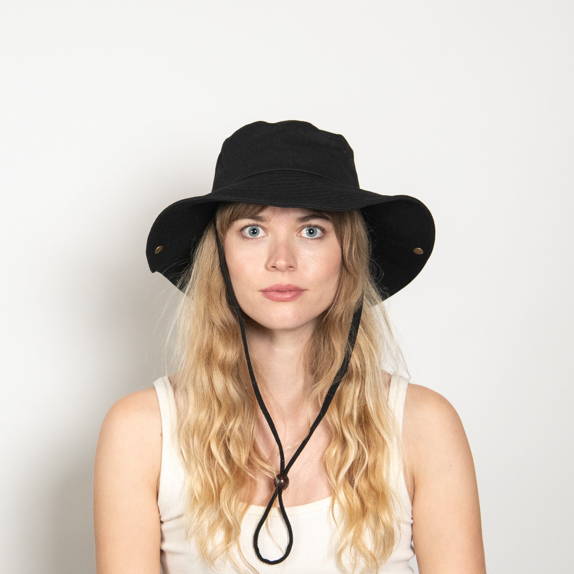 Woman wearing a black wide-brimmed hat with a chin strap on a light background