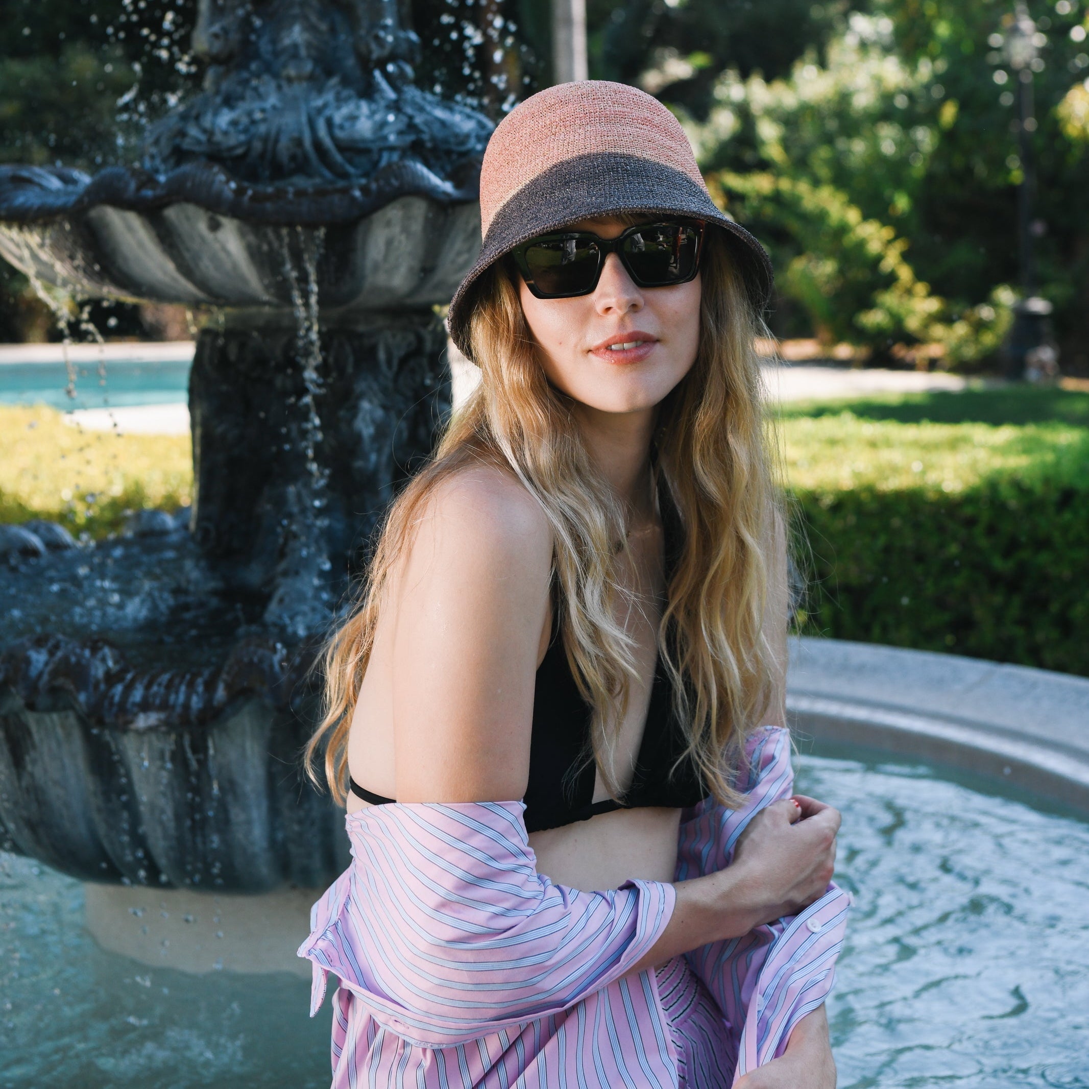 Woman wearing a hat and sunglasses in front of a fountain