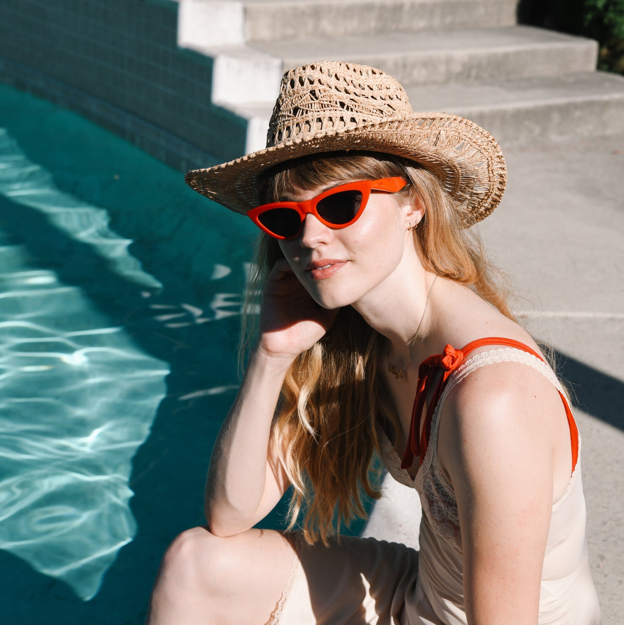 Woman wearing a straw hat and red sunglasses by a pool