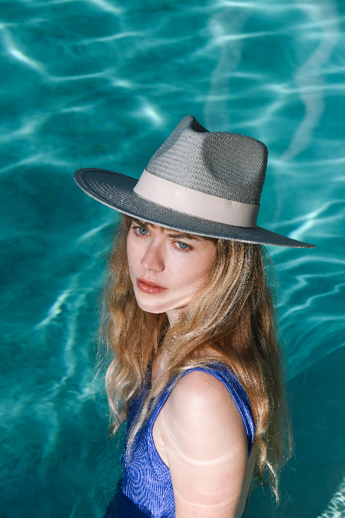 Woman wearing a black hat with a white band against a blue water background