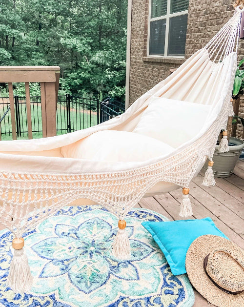Hammock on a wooden deck with a rug, pillow, and hat in the foreground.