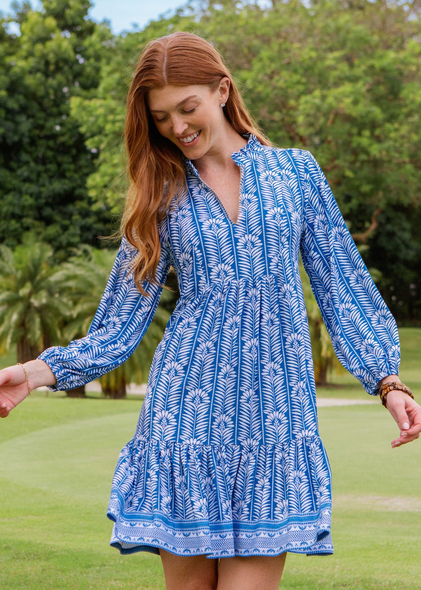 Woman wearing a blue patterned dress standing on grass with trees in the background