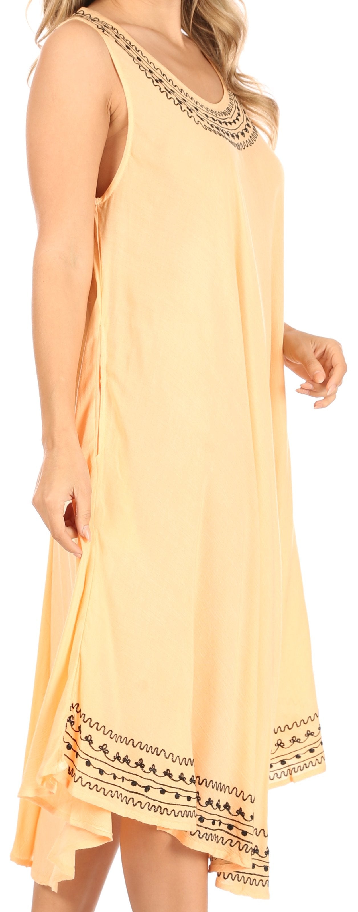 Woman wearing a light yellow dress with black embroidery details on a plain background