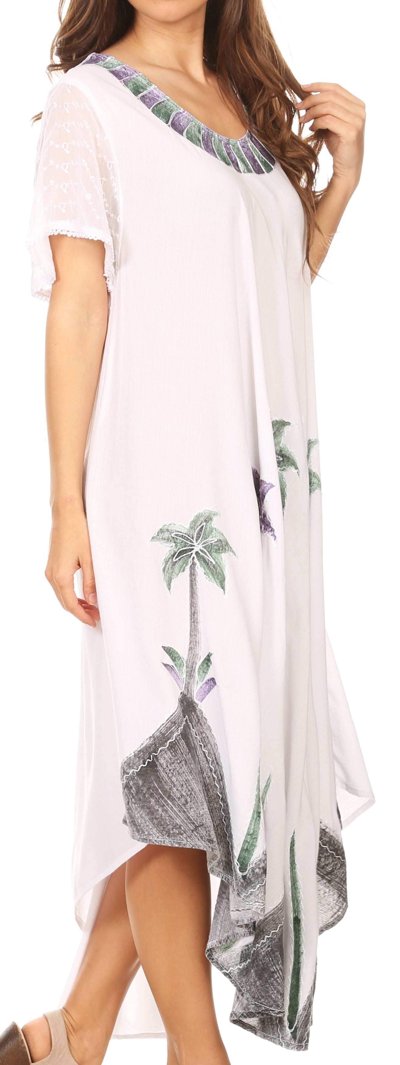 Woman wearing a white dress with palm tree designs, standing against a plain background.