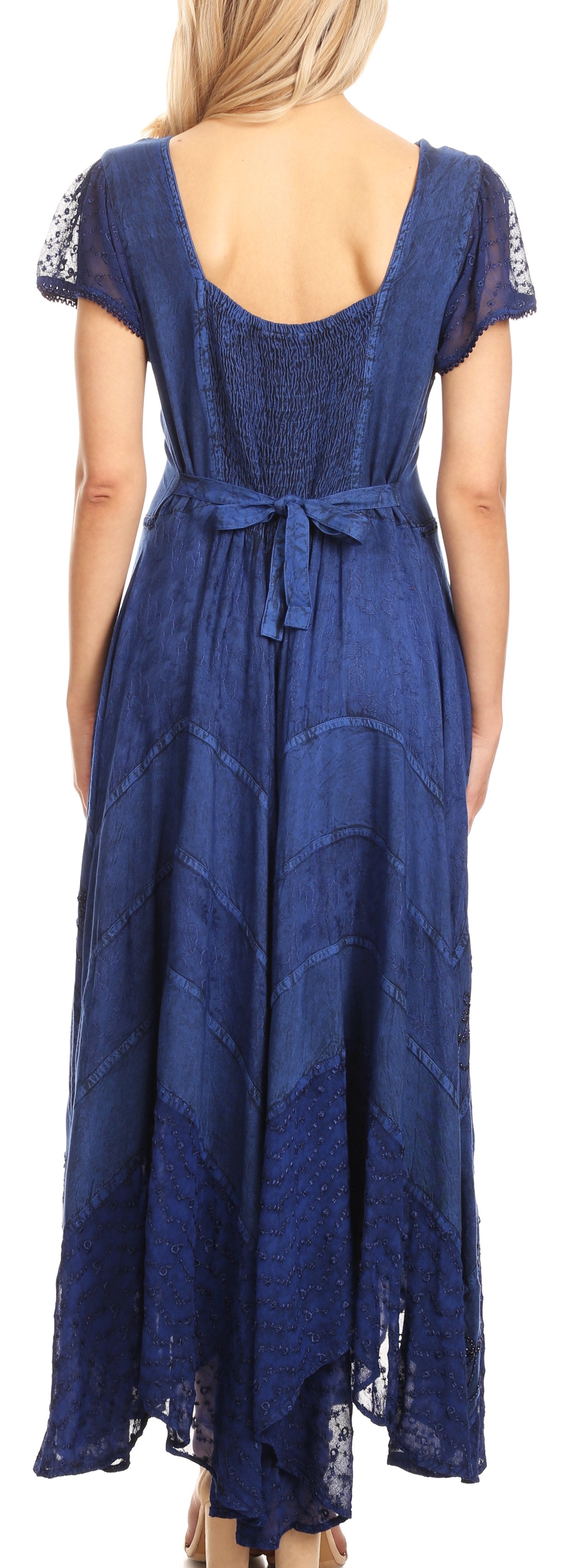 Woman wearing a long blue dress with lace details, standing against a plain background.
