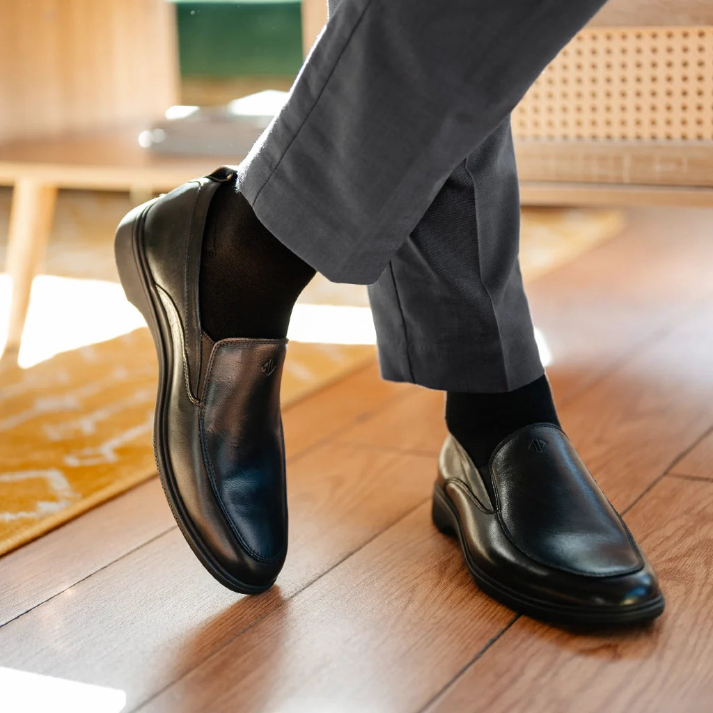Person wearing black dress shoes and gray pants on a wooden floor.