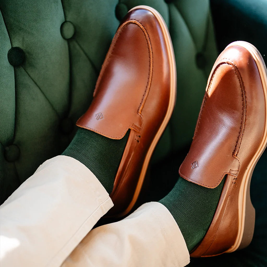 Brown leather loafers worn with green socks and beige pants on a green textured background