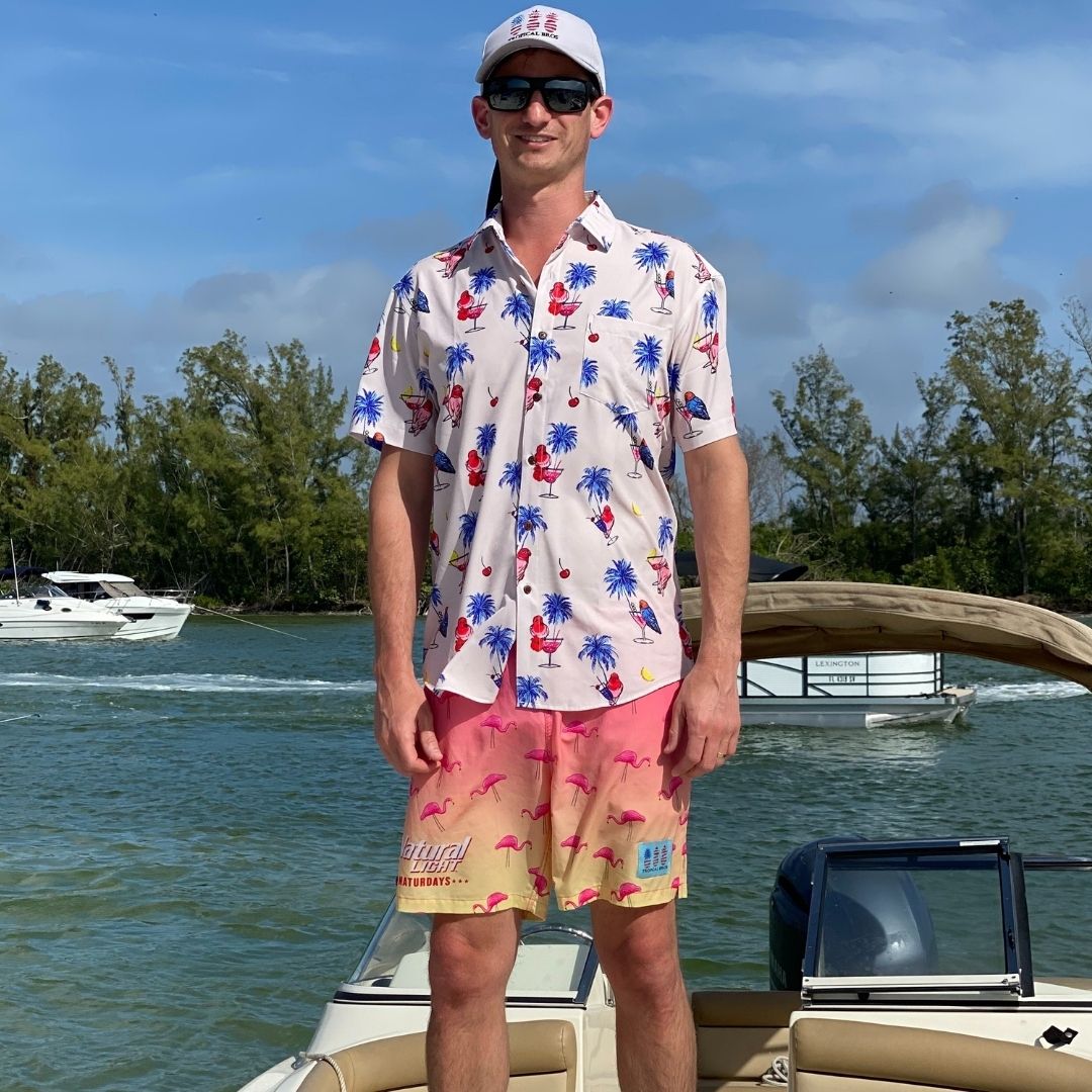 Man in a colorful shirt and shorts standing on a boat with a scenic background