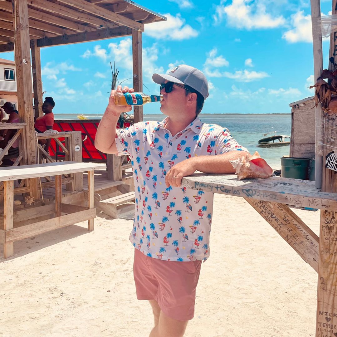 Man drinking a beer on a beach with wooden structures and water in the background