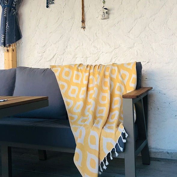 Yellow patterned towel draped over a gray sofa with a white textured wall in the background.