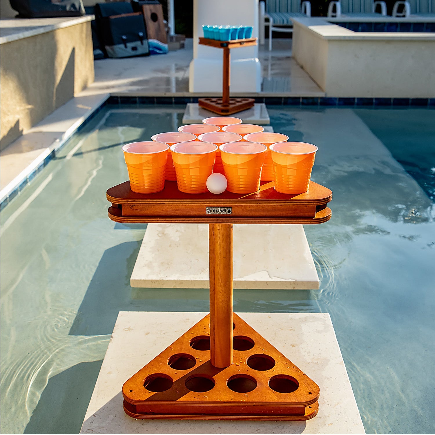 Wooden beer pong table with orange cups and a ball by a pool