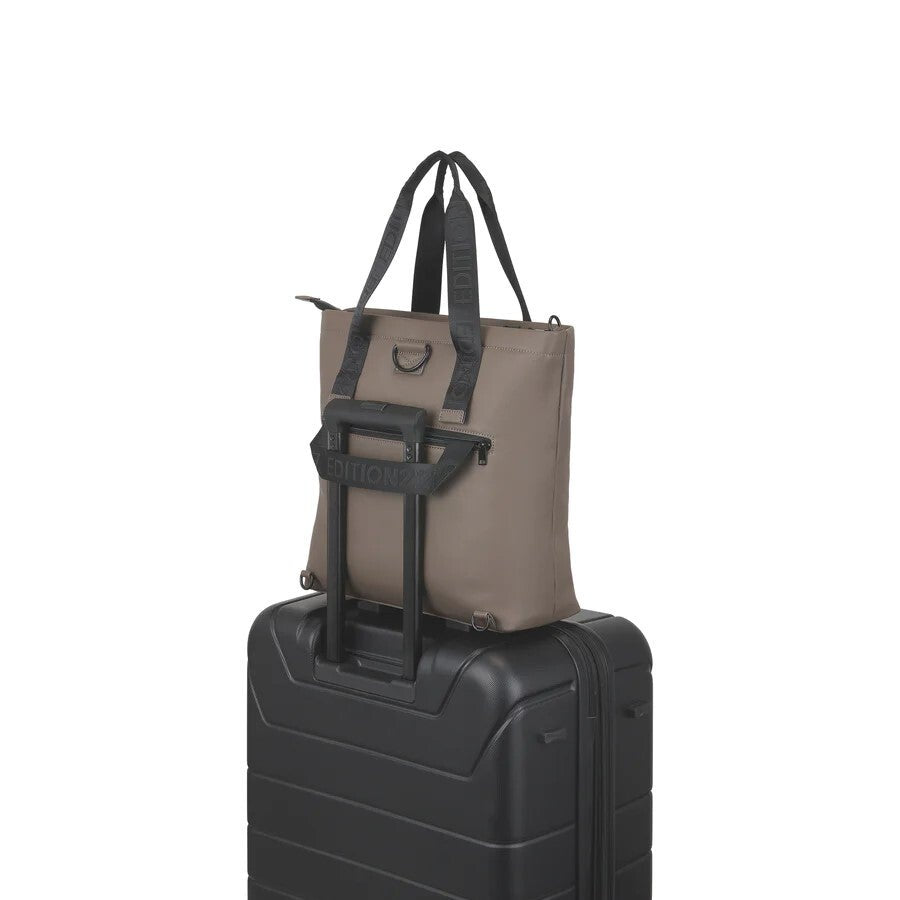 Brown tote bag with black straps on a black suitcase against a white background