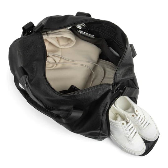Black duffel bag with white sneakers and beige clothing on a white background