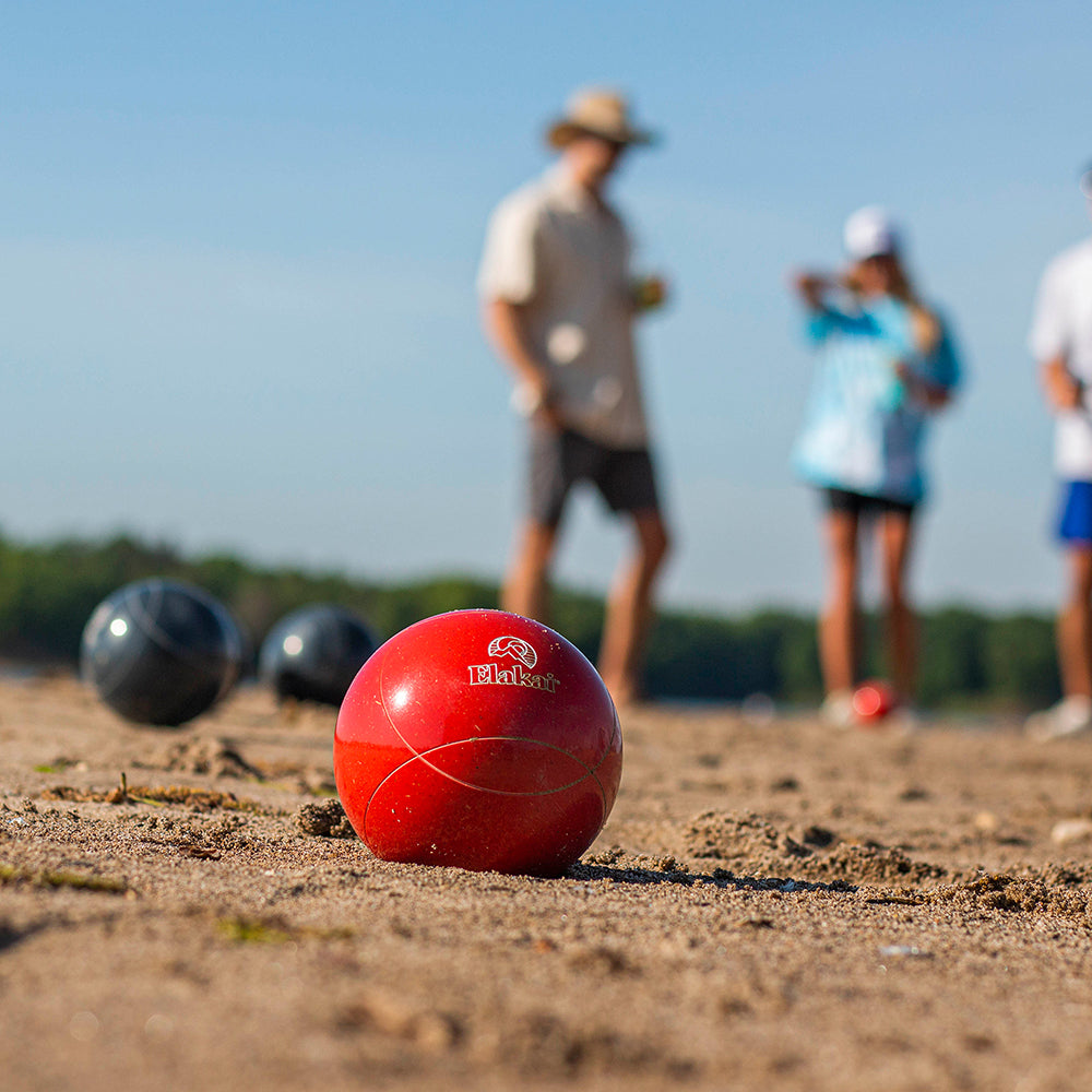 Red bocce ball on a sandy surface with people in the background