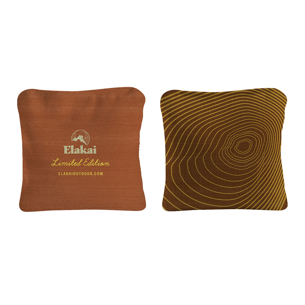 Two decorative pillows, one brown with Elakai branding and one with a wavy pattern, on a white background.