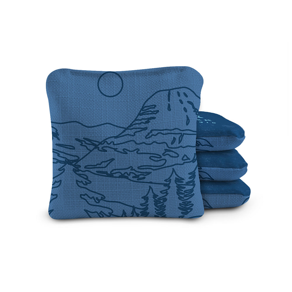Blue cornhole bags with mountain design on a white background