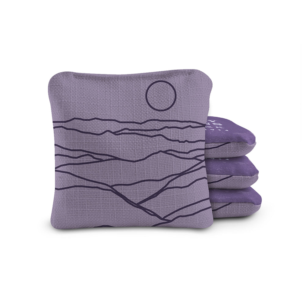 Purple cornhole bags with mountain and sun design on a white background