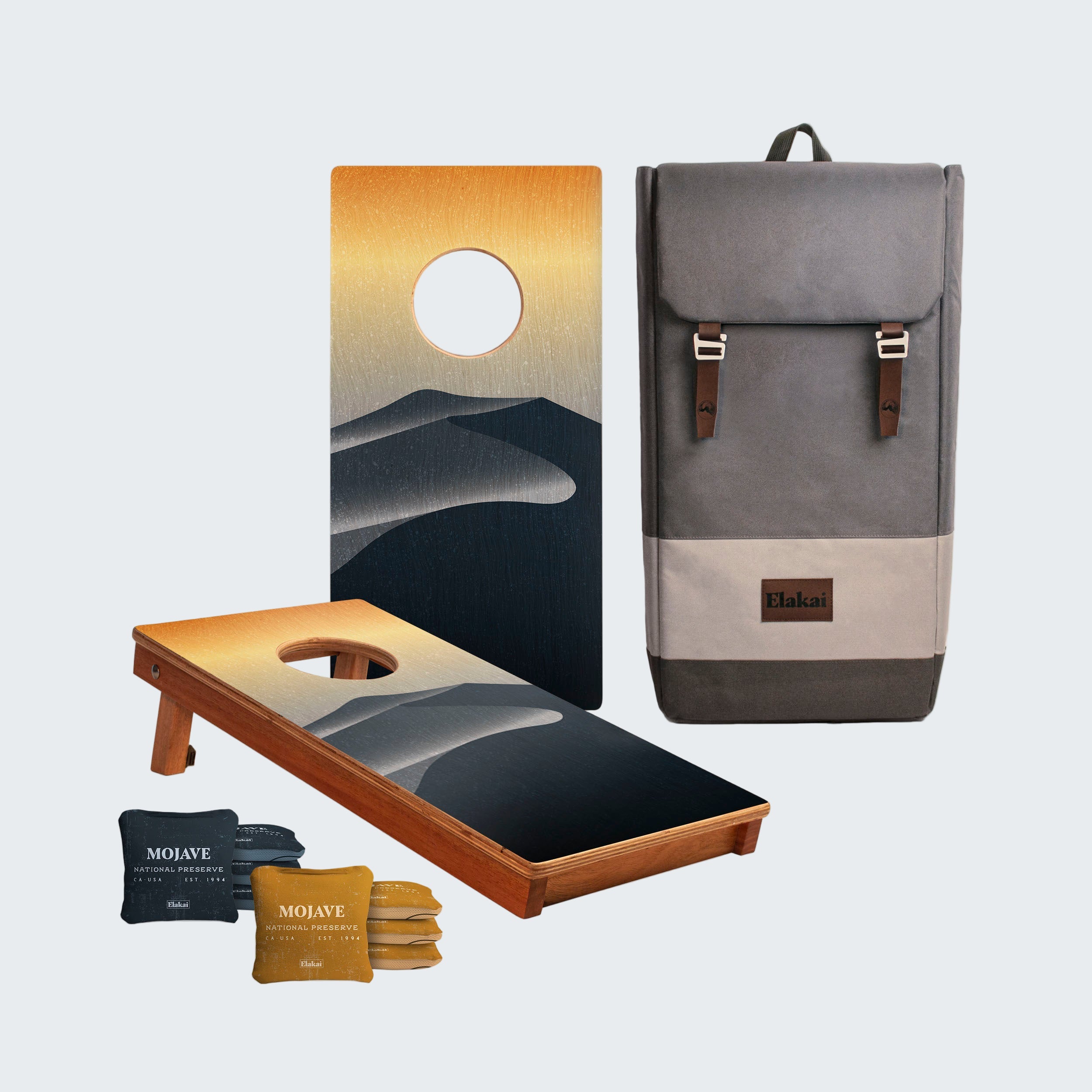 Cornhole board with mountain design, gray backpack, and bean bags on a white background