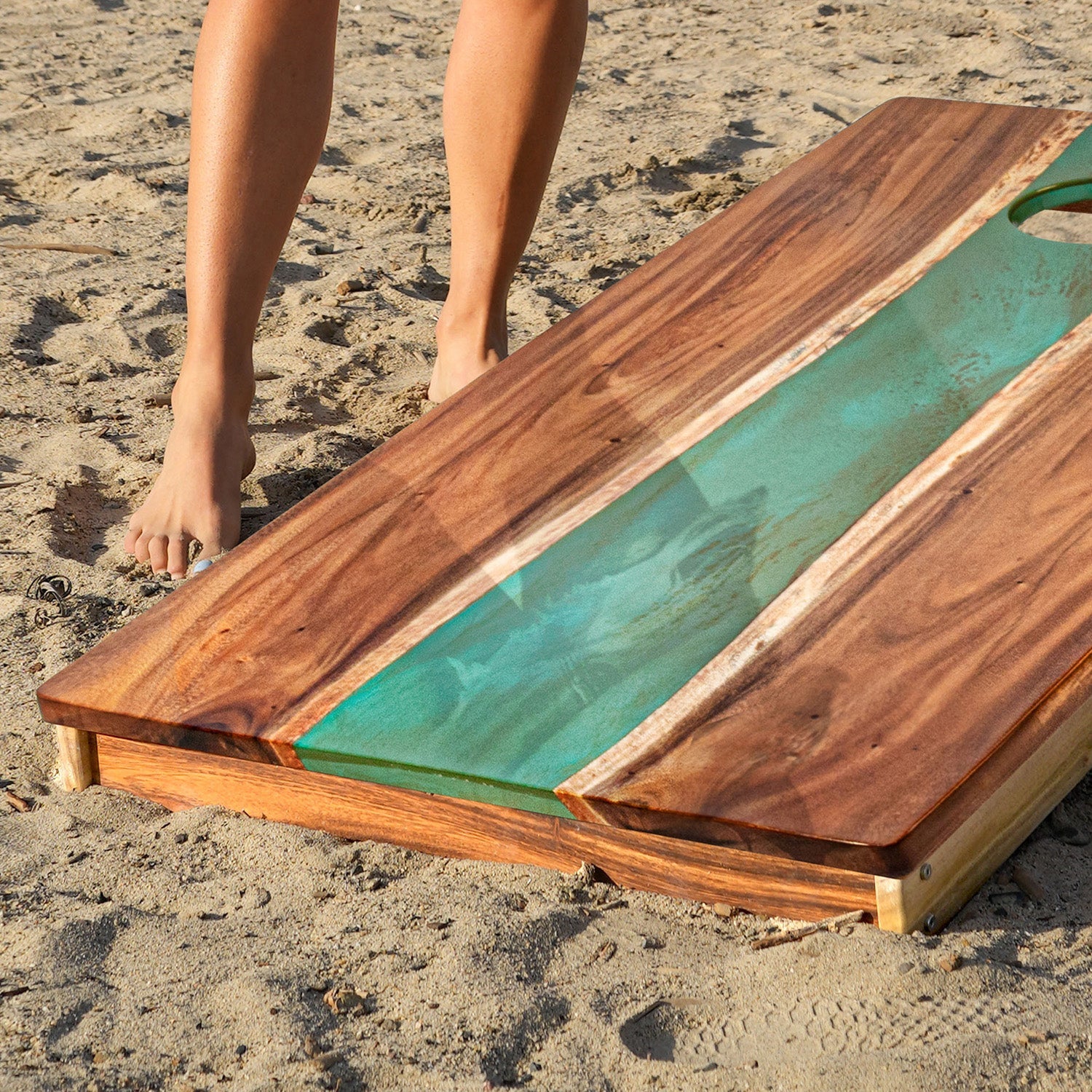 Wooden cutting board with green resin on a sandy surface