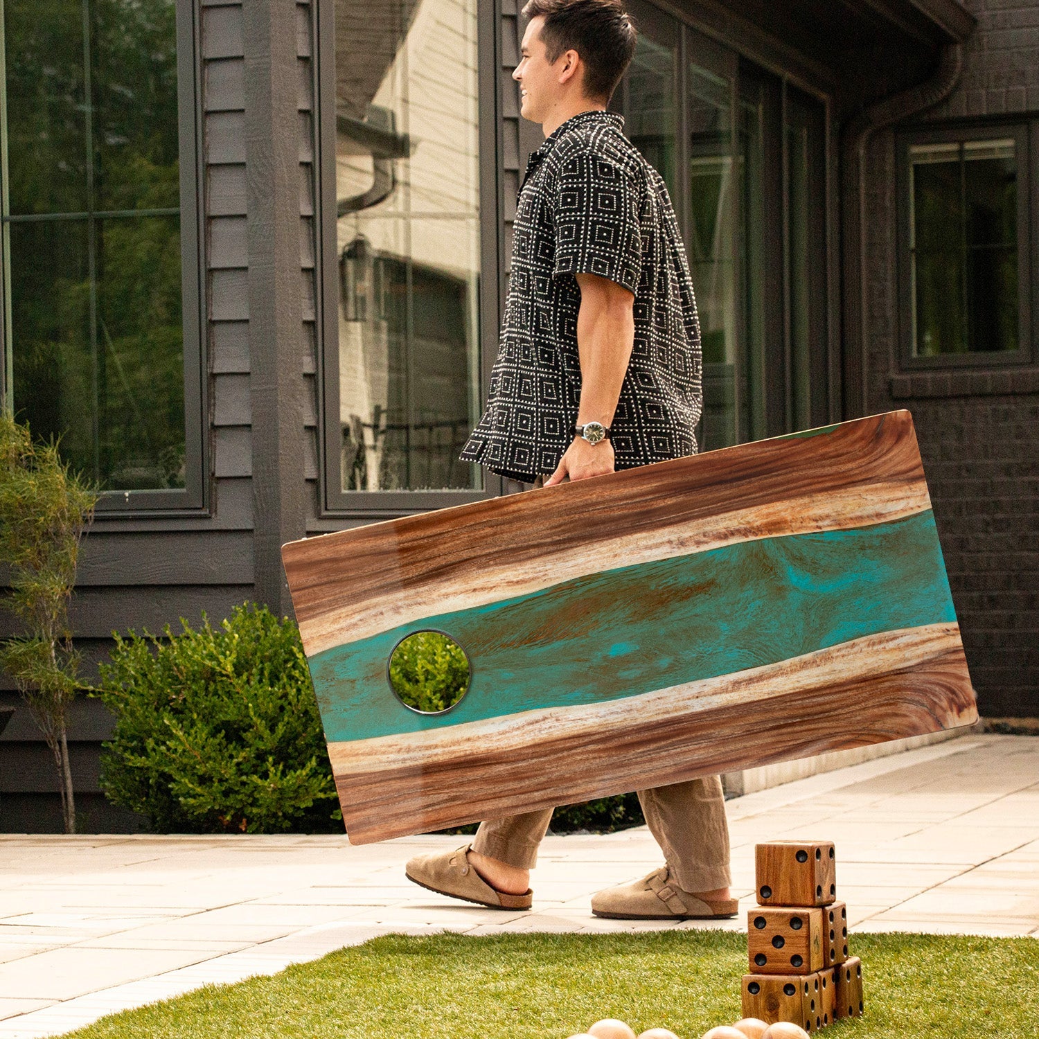 Man holding a large wooden board with a blue and brown design outdoors.