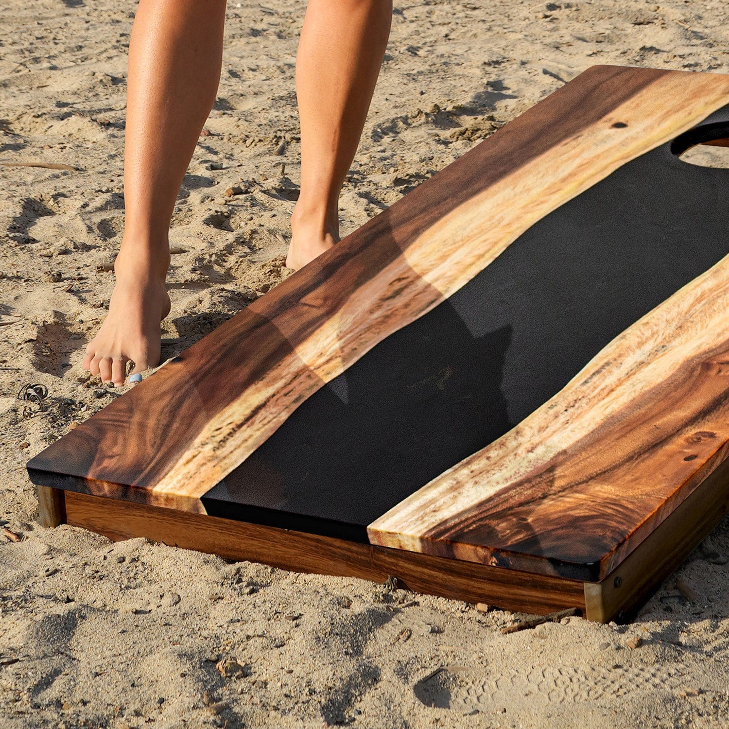Wooden cornhole board on sand with a hand reaching towards it