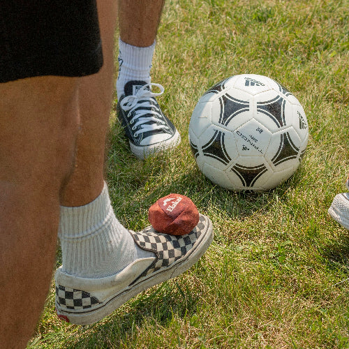 Person wearing checkered shoes on grass with a soccer ball and red object nearby