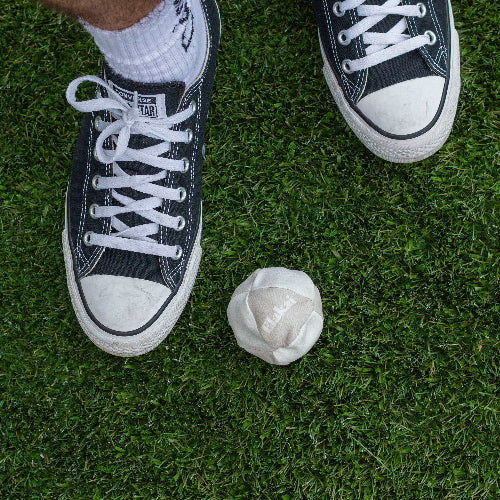 Black sneakers with white laces on grass next to a white ball