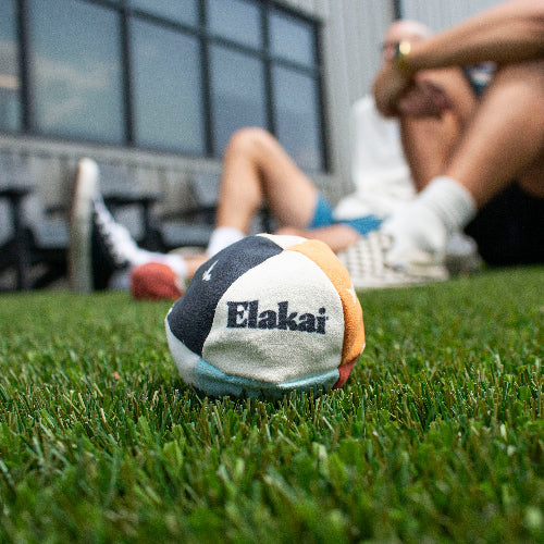 Colorful beach ball with 'Elakai' branding on grass, person sitting in background