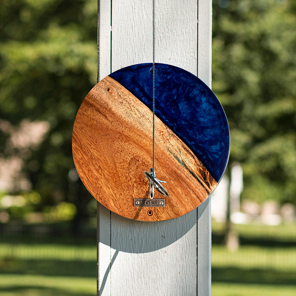 Wooden and blue circular ornament hanging on a wooden post with a blurred green background