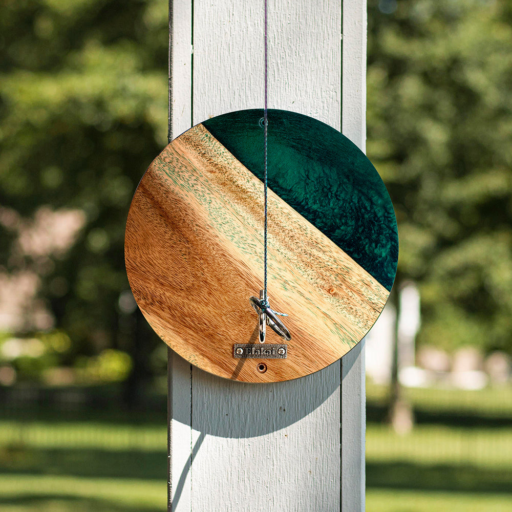 Wooden and green circular wind chime on a post with a blurred green background