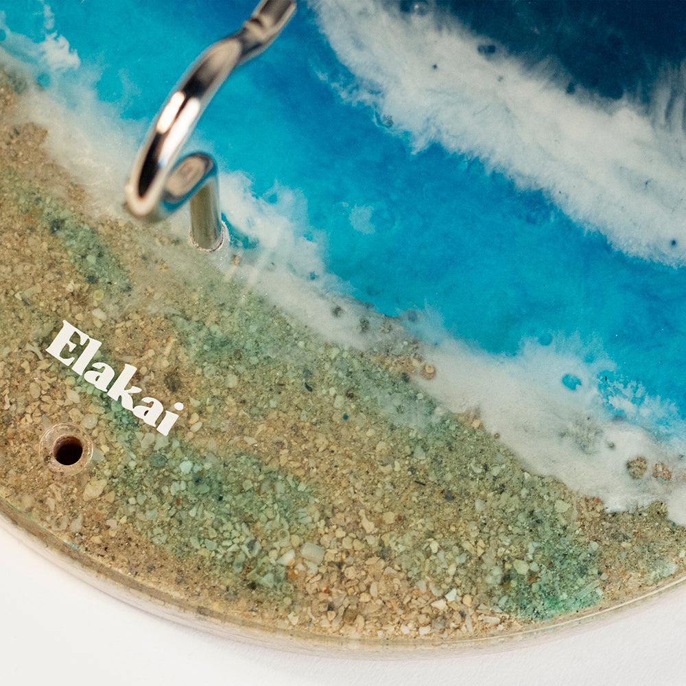 Close-up of a surfboard with 'Elakai' branding on a beach setting.