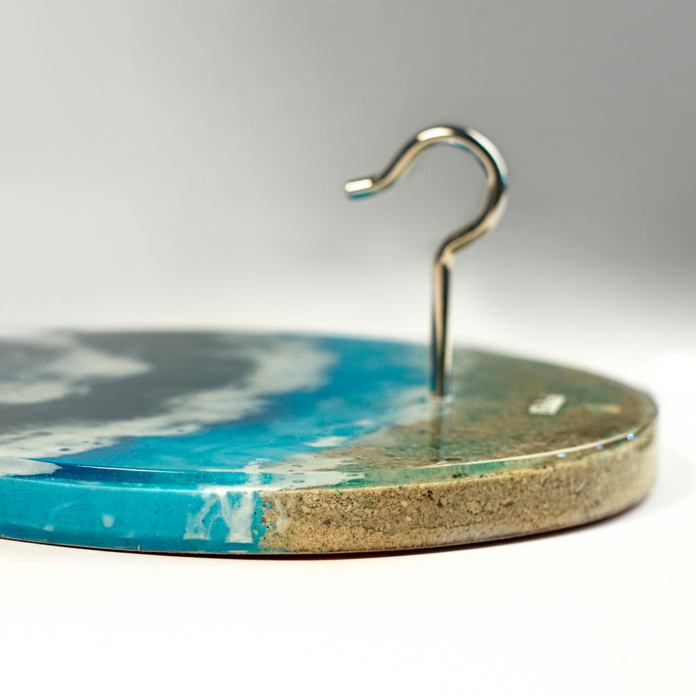 Round tray with blue and beige design and a metal hook on a gray background
