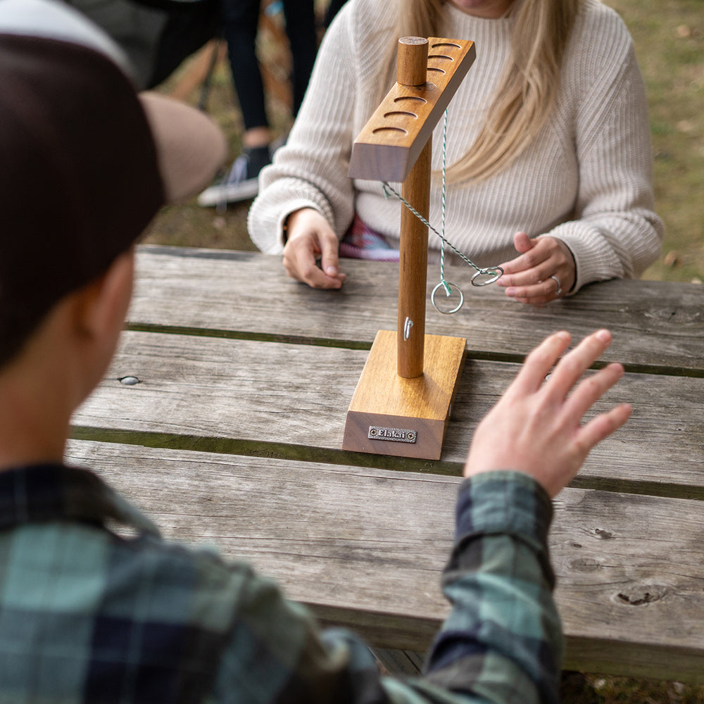 Two people playing with a wooden fishing game on a wooden table outdoors.