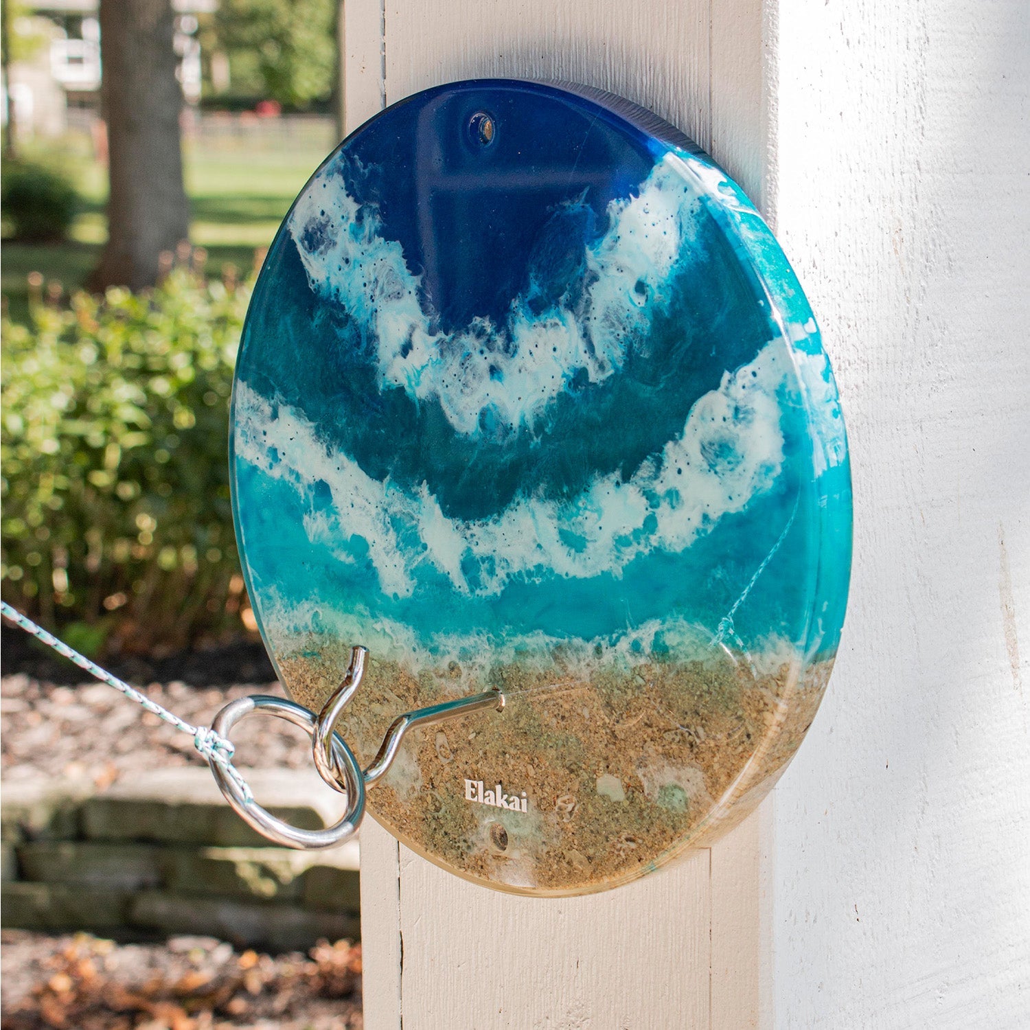 Decorative plate with blue and green design hanging on a white wall outdoors.