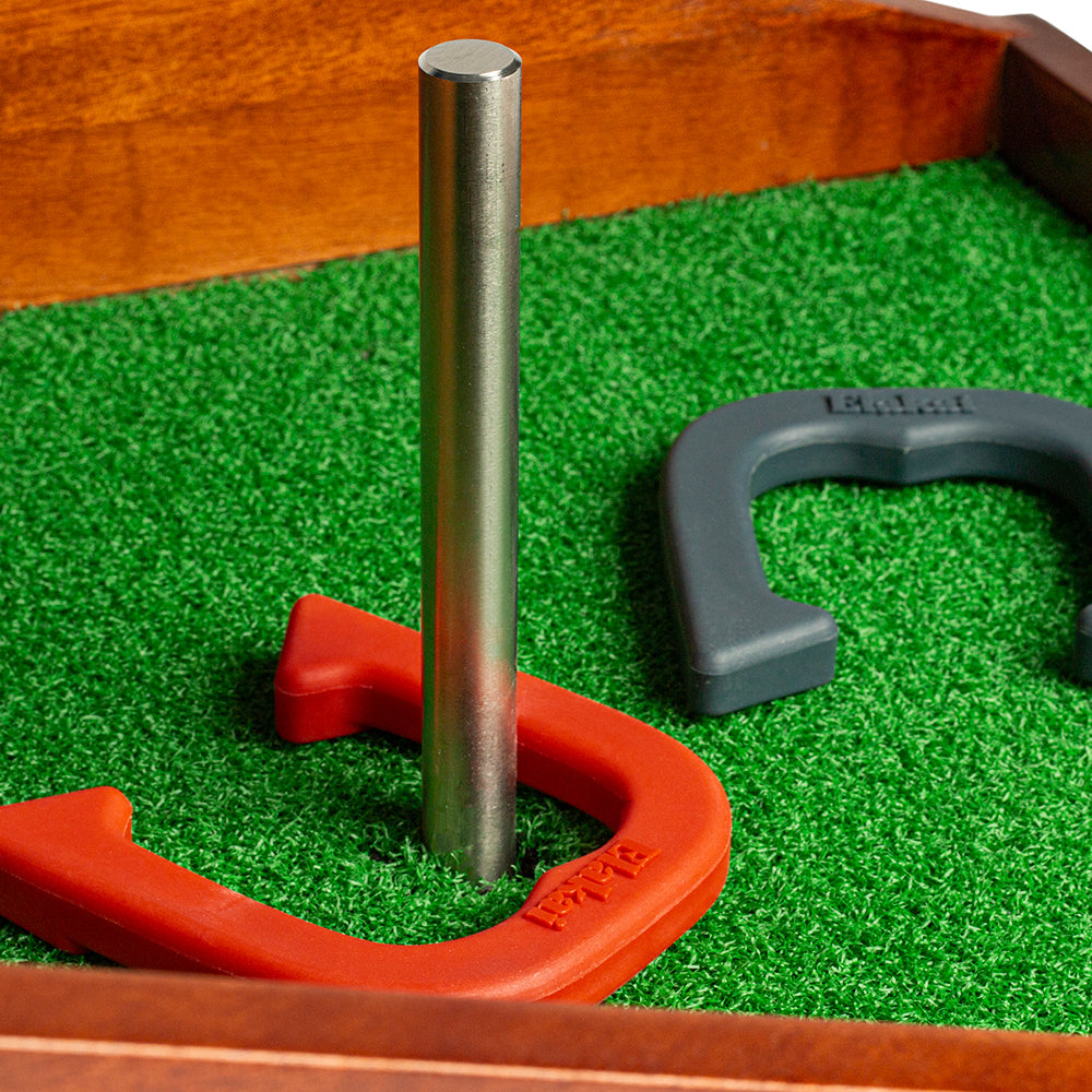 Horseshoe on a green surface with a metal stake and wooden border