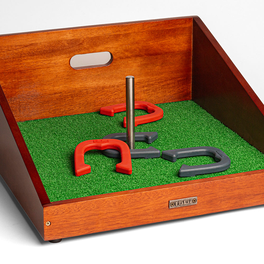 Wooden tray with a green grass-like surface and red and gray horseshoe game pieces.