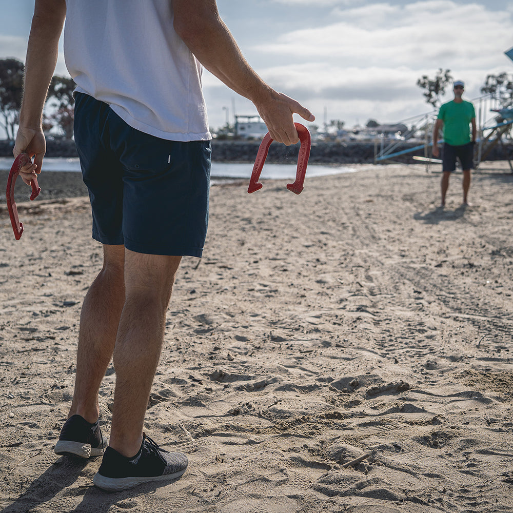 Person on a beach holding red hula hoops with another person in the background